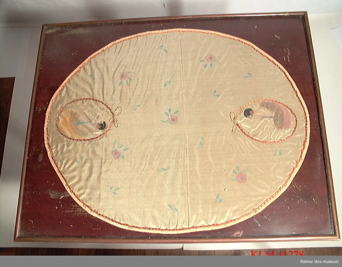 KLM 41278. Bord. Av trä. Rektangulärt, en hylla undertill. Skivan täckt med en glasskiva, under den ligger en oval duk av gult tyg med broderat motiv: blommor och två medaljonger med damer.