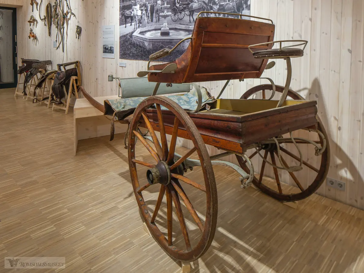Fra utstillingen "i vognskjulet". Skysskjerre fra Fuglset.Denne skysskjerra ble laget av K. A. Mork mellom 1910 og 1915. Han hadde sitt snekkerverksted på garden Mork ved Hjelset. Kjerra har plass til 2 personer i setet og en «vognmann» bak på «kuskesetet». Denne typen hestekjøretøy var svært vanlig i vårt distrikt rundt 1900. Kjerra ble gitt til Romsdalsmuseet av Magnar Fuglset i 1960. Magnar Fuglset drev en oksestasjon inne på garden Vårtun på Nedre Fuglset. Han drev også med hesteskyss.