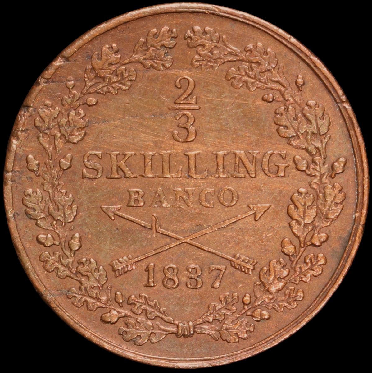 Mynt med valören 1 skilling banco. Åtsidan har en bild på Kung Karl XIV Johan. Frånsidan visar valören, två korslagda pilar samt en växtkrans.