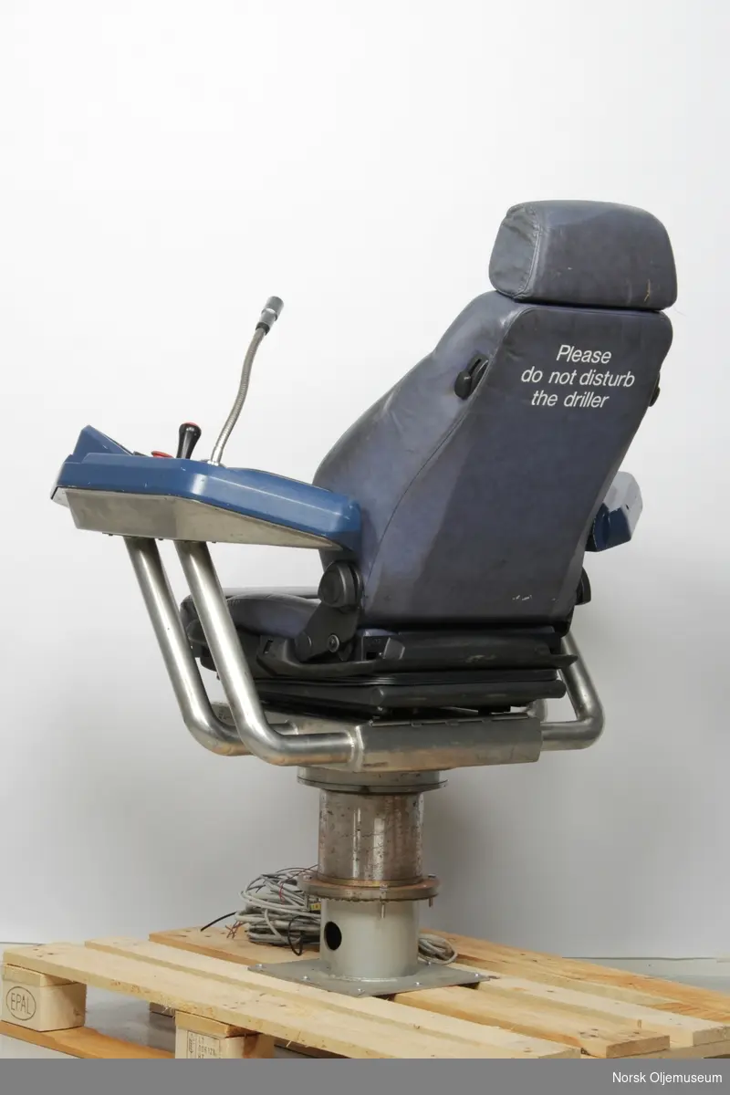Operatørstol som er utstyrt med styrespaker og knapper for fjernstyring og mikrofon på armlener.