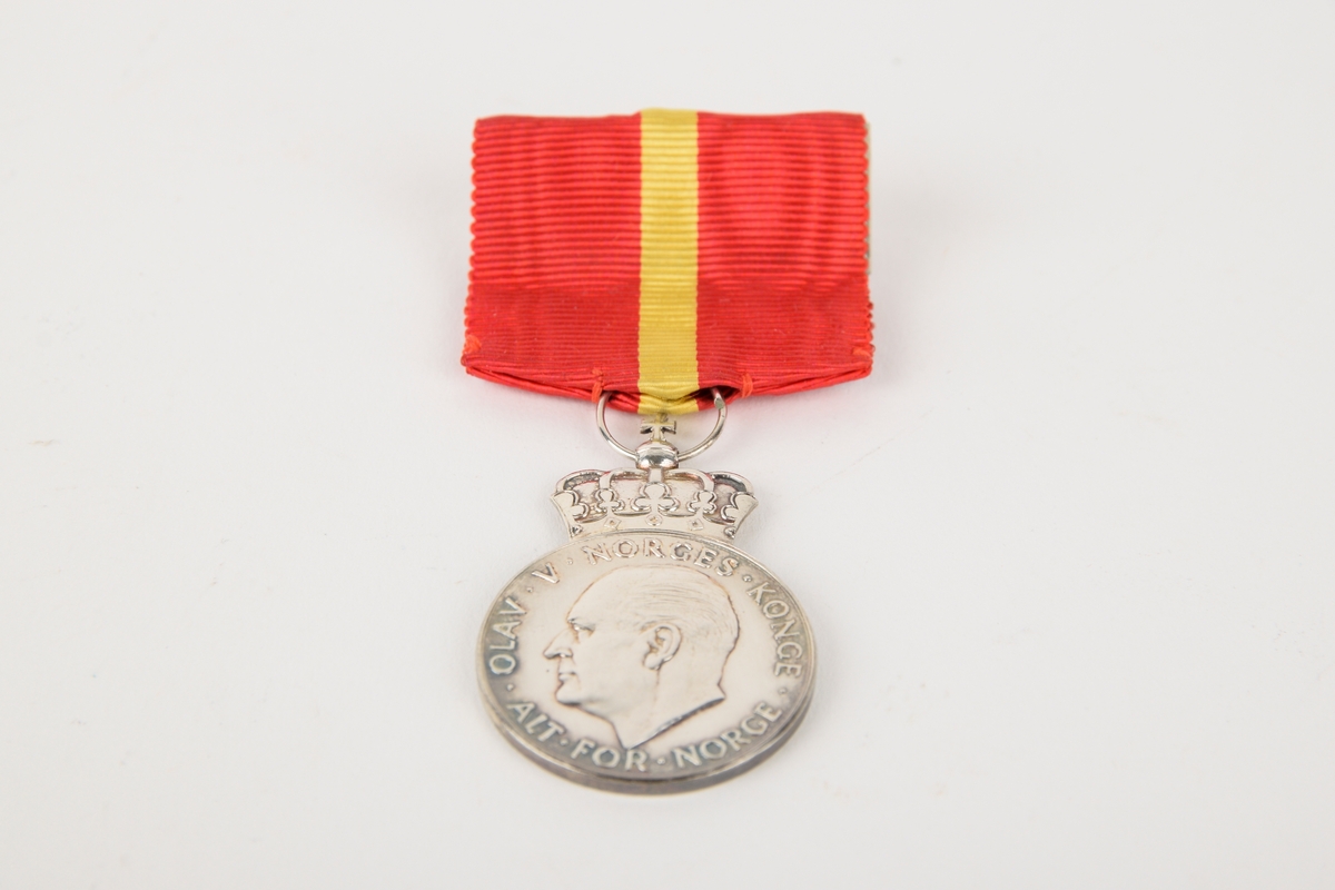 Et eksemplar av "Kongens fortjenstmedalje" i originalt etui. 

Sirkulær medalje med ordensbånd, oppbevart i rektangulært etui. Etuiet har motiv av en krone i sølv på lokket.
