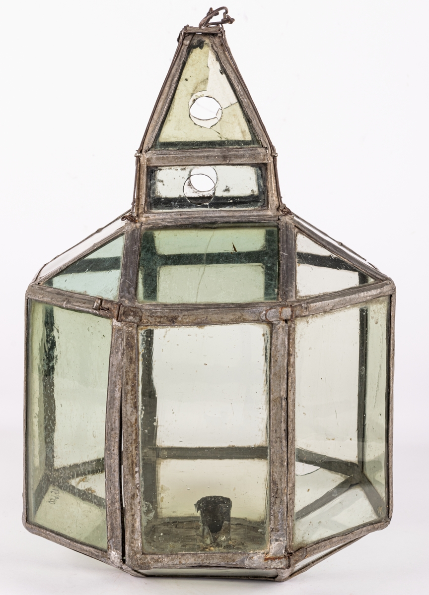 Lykta av glas med blyspröjsar emellan. 8-sidig med liten fyrsidig lanterning överst. Bottenstycke av plåt med hållare för ett ljus.
