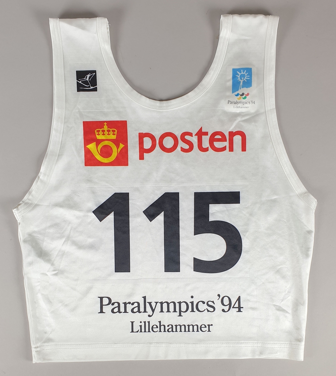 Hvit startnummer, nummer 115. Påført Postens logo, emblemet til Paralympics i 1994 og piktogrammet for Langrenn.