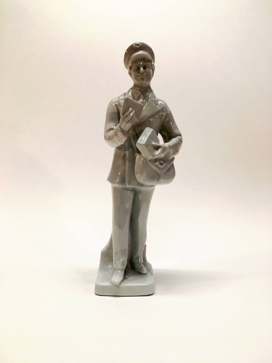 Figurin förställande en man i uniform med mössa och brevbärarväska. Han håller ett brev.
