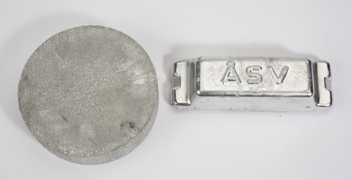 Aluminiumsbare med bokstavene ÅSV støpt inn på oversiden. Ligger i etui med reklamehefte