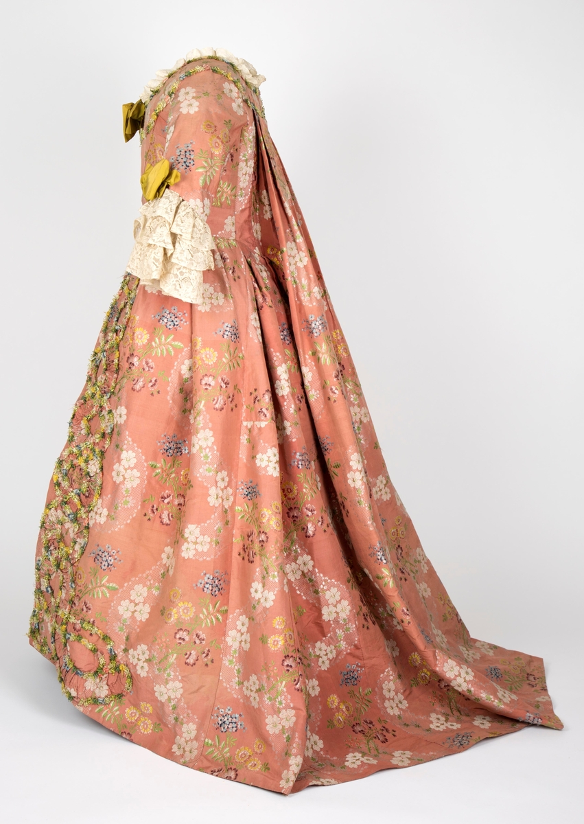 Overkjole av silkebrokade med tilhørende skjørt av samme materiale, begge prydet med blomsterranker av possement. Watteau-folder. Se undernummer.