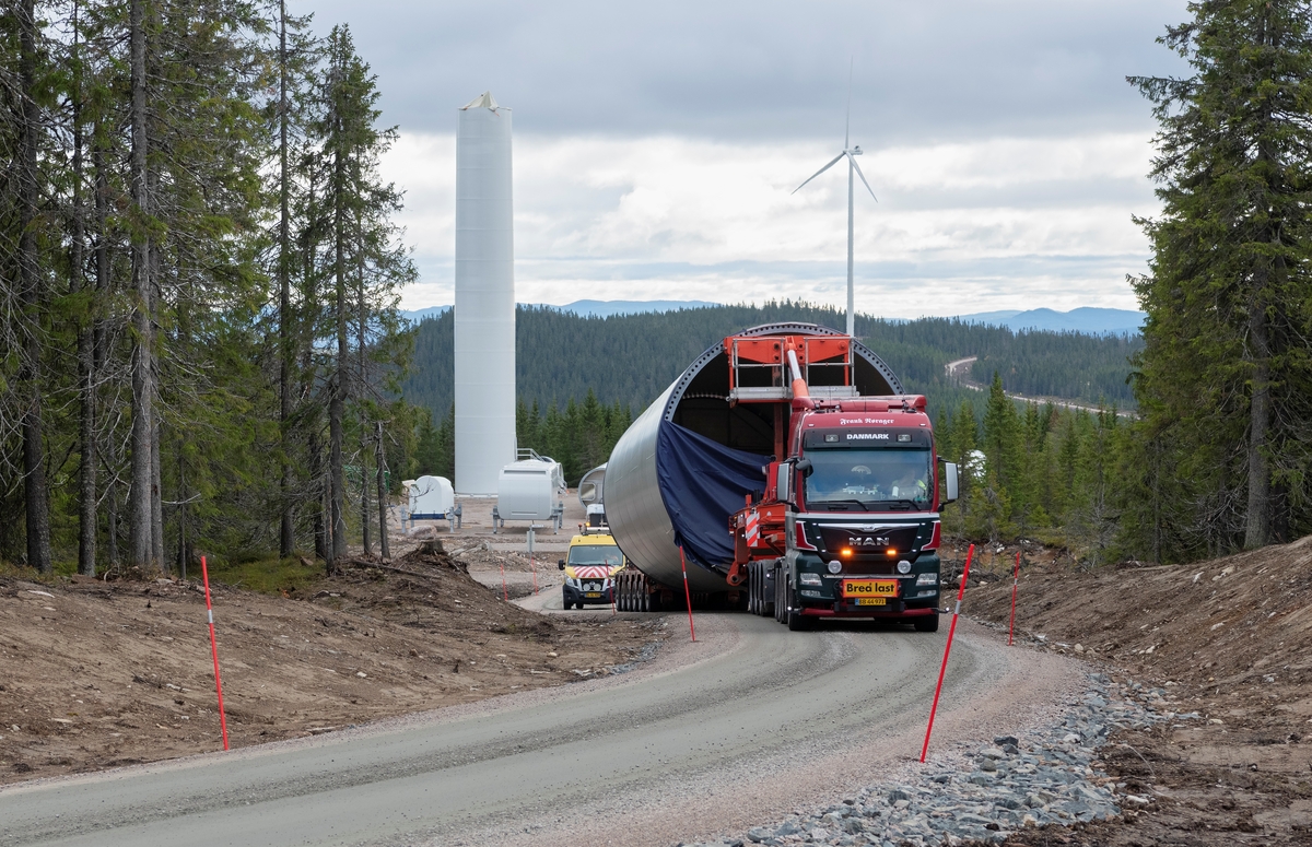 Bygging av vindkraftverk på Finnskogen, Hedmark. Transport av et element som skal bli en del av turbinkroppen i en vindturbin. Kjølberget Vindkraftverk, Våler kommune, Innlandet. I bakgrunnen ser vi en ferdig montert vindturbin ved Buberget sør i anlegget, samt en turbin under oppføring.