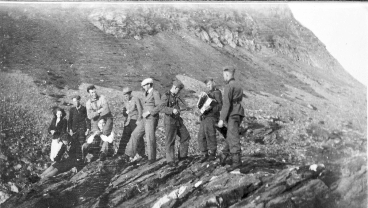 Tyske soldater og norske sivile fotografert på en bergknaus på Indre Elgsnes. Fjell i bakgrunnen.