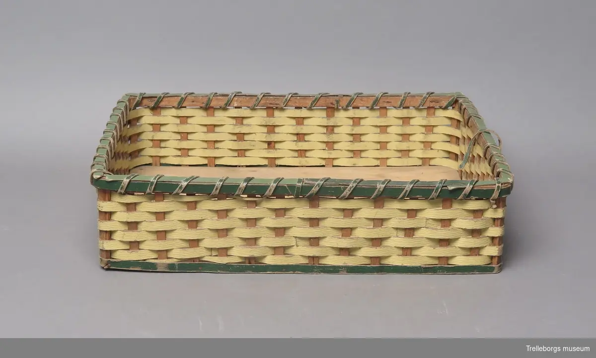 Botten av trä, med sidor av pressat papper som flätats på stomme av trä.
Sidorna är gulmålade, med grön kant upp- och nedtill.