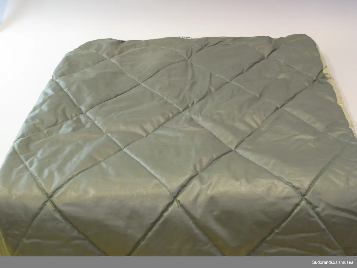 Tynn grønn sovepose i vattert bomull og med vanntett stoff på undersiden. Glidelås i øverste del av soveposen.