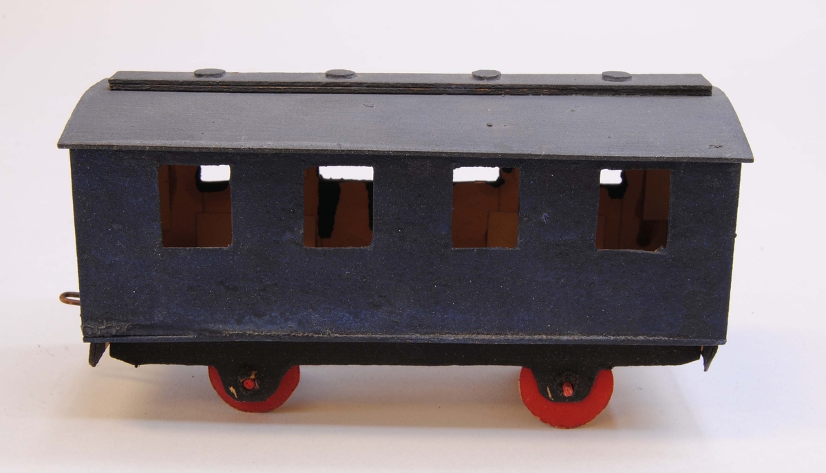 Blå personvagn av papp.
Delarna är limmade eller sammanfogade med rött lack. Hjulen är gjorda av papp och hjulaxlarna av fyrkantiga träpinnar, troligtvis tändstickor. Vagnen är målad blå med mörkgrått tak, svart underrede och röda hjul. Under vagnen är datumet "30/3 1919" handskrivet.
På ena kortsidan av vagnen finns böjd ståltråd, en ögla för att koppla samman vagnen med andra vagnar eller lok. På andra sidan finns spår av att det antagligen har suttit en krok. Vagnen har ett välvt tak med en avlång rektangel i mitten med fyra runda upphöjningar som föreställer lamphuvar och fyra fönster på varje sida av vagnskorgen.