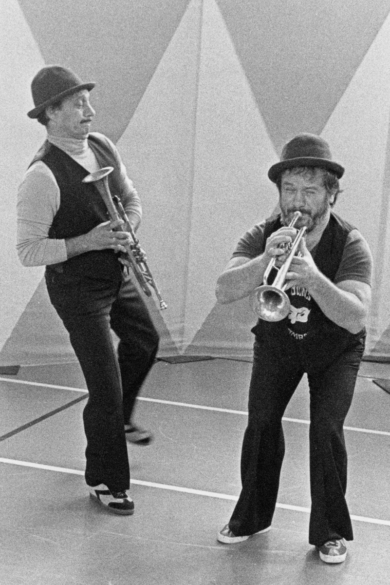 Två män i hatt och med varsin trumpet. Den ena spelar på trumpeten. Personerna är Clownerna Colombaioni vid namn Romano och Mario.