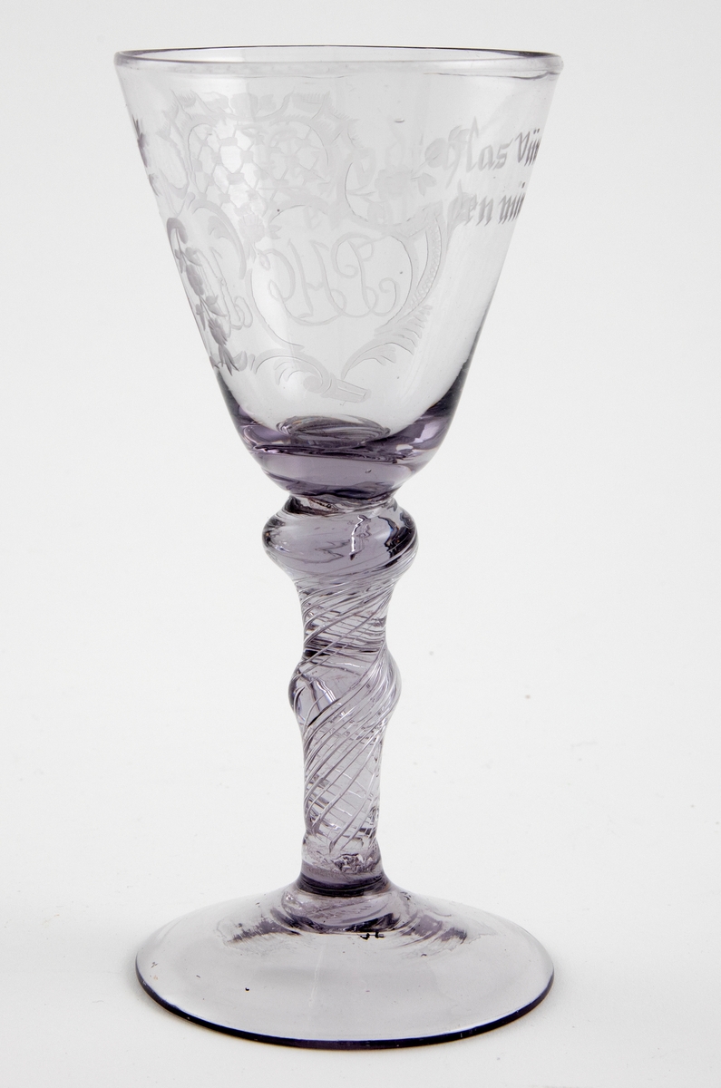 Chrystal Desert vinglass i klart glass med svak lillafarge. Konisk kupa som hviler på en stett med to vulster samt luftspiraler. Dekorert med graverte initialer i rokokkokartusj samt skålevers.