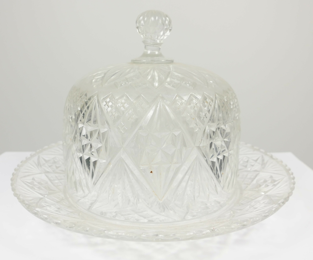 Rund glassklokke av glass med håndtak midt på øverst, klokken står på en rund skål av samme materiale og med samme dekor. 