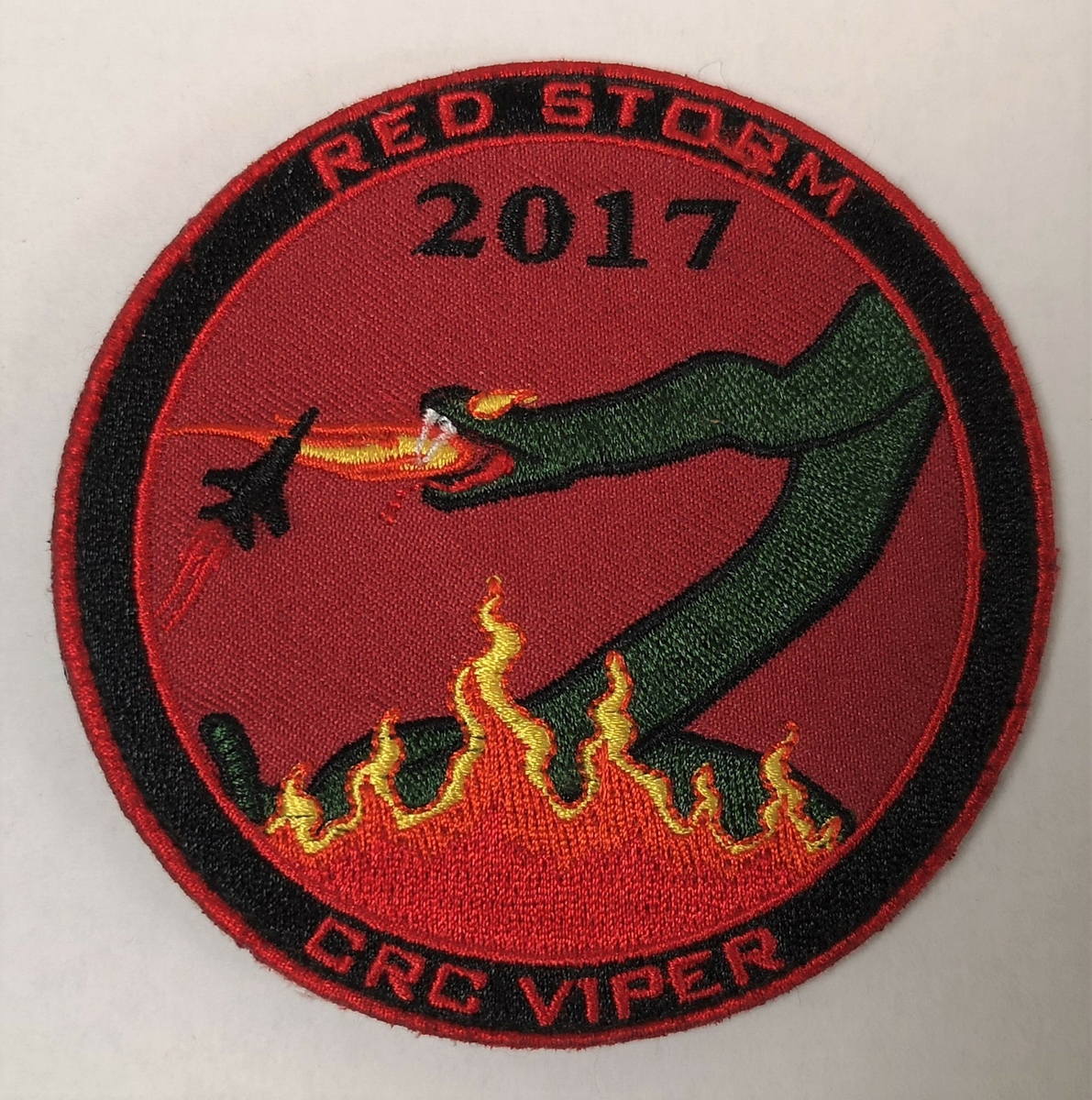 Motivet er en grønn slange (Viper) som stiger opp av et flammehav og fanger et jagerfly på rød bakgrunn.

