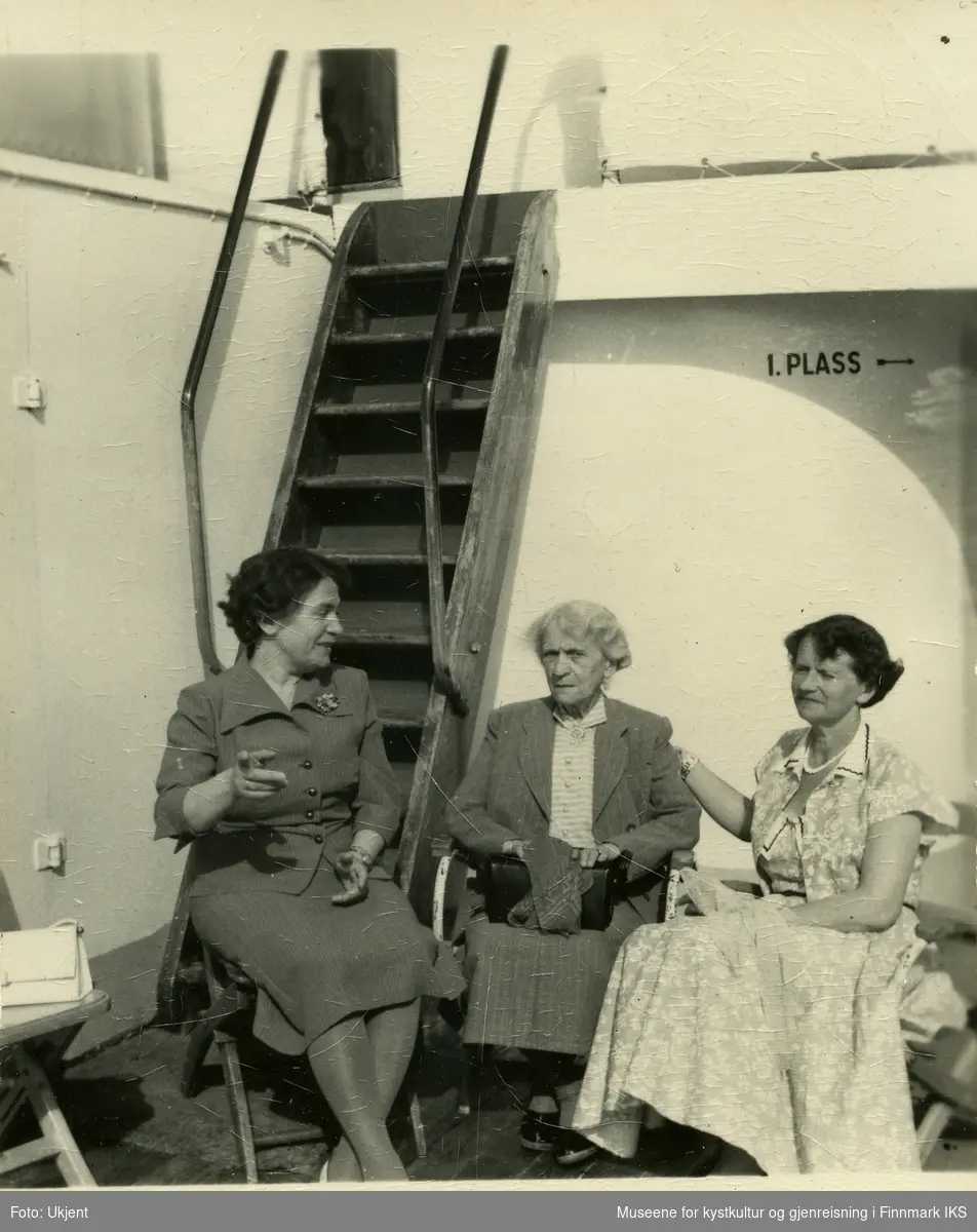 Tre kvinner sitter på dekk til et skip og samtaler.