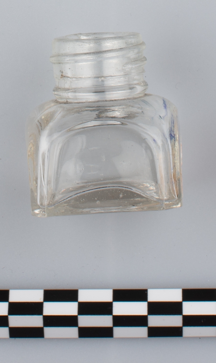 Blank, tom flaske i klart glass uten skrulokk. del av etikett på en side. Rester av blå substans på innsiden. Etiketten har orange bakgrunn
