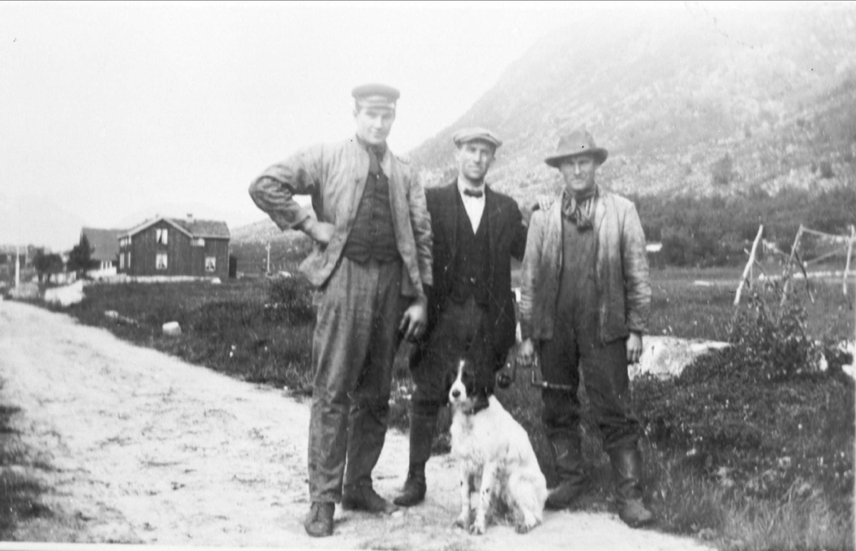 Amatørportrett av tre menn med en hund på en gårdsveg.