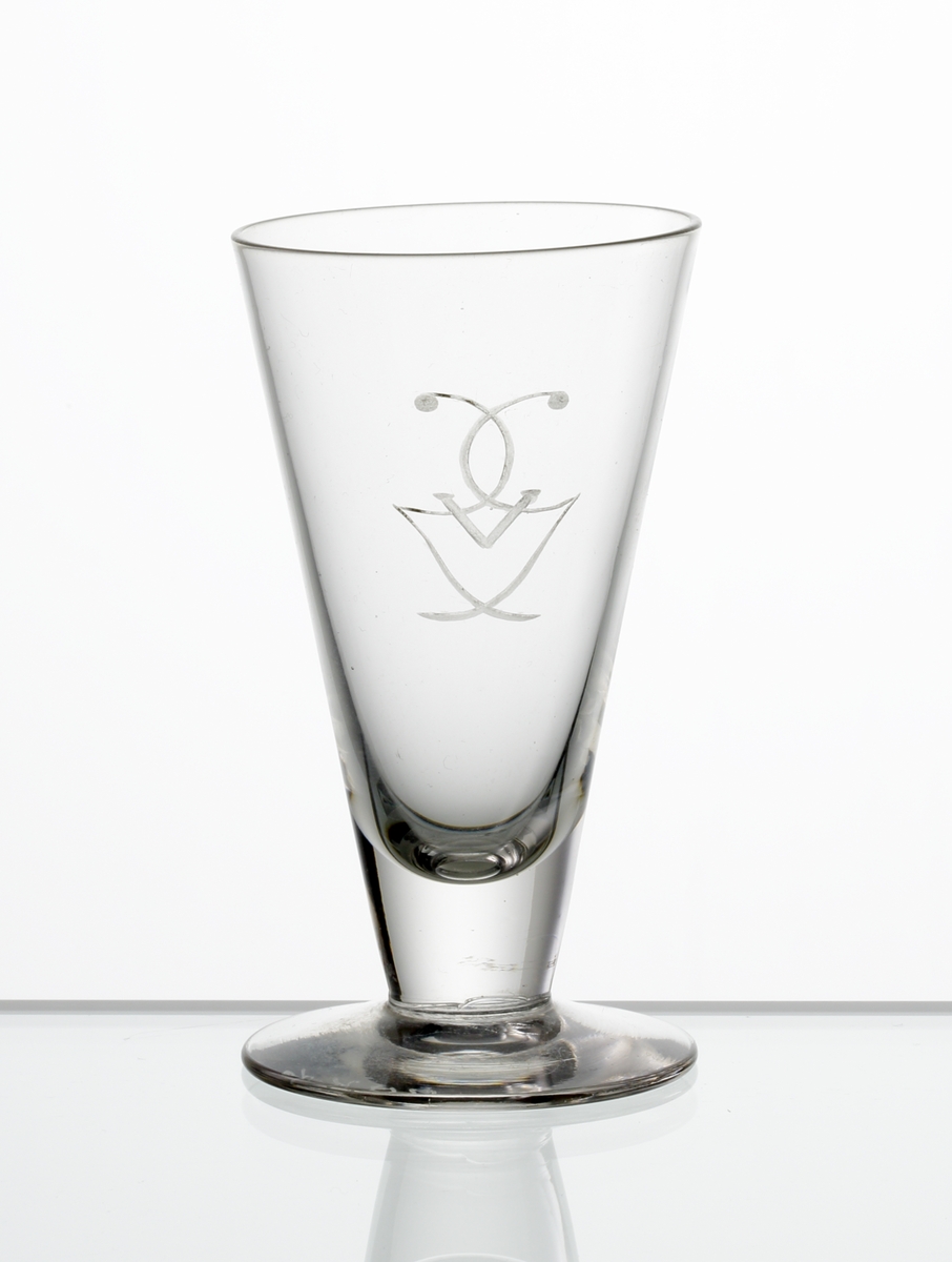 Design: Edward Hald.
Brännvinsglas. Konisk kupa på fot, med graverat monogram (Gustaf V). 

Gustaf V (1858-1950), kung av Sverige 1907-1950.