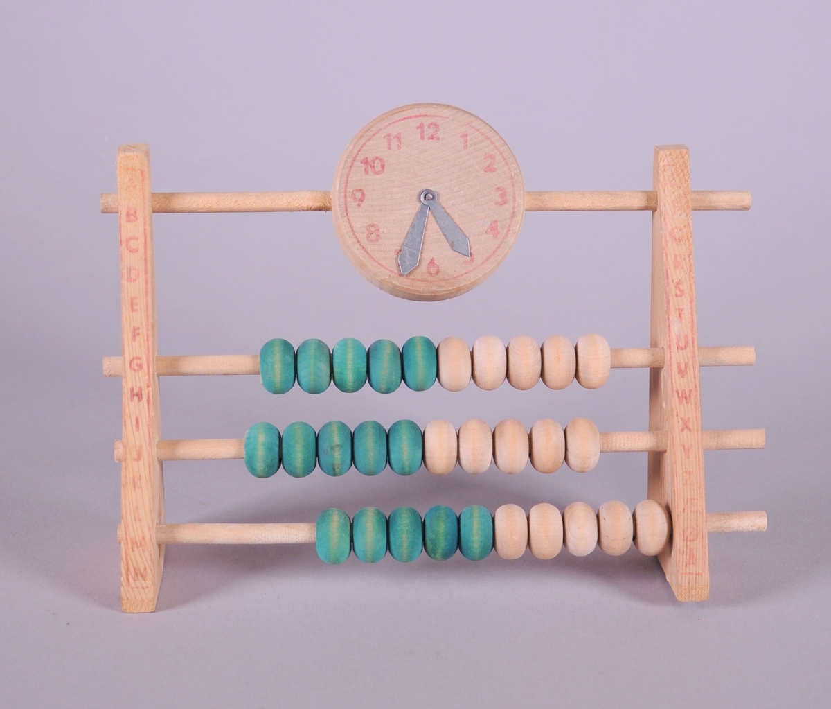Kuleramme av tre, med klokke og grønne og trefargede kuler. Alfabetet er skrevet på hver side av kulerammen.