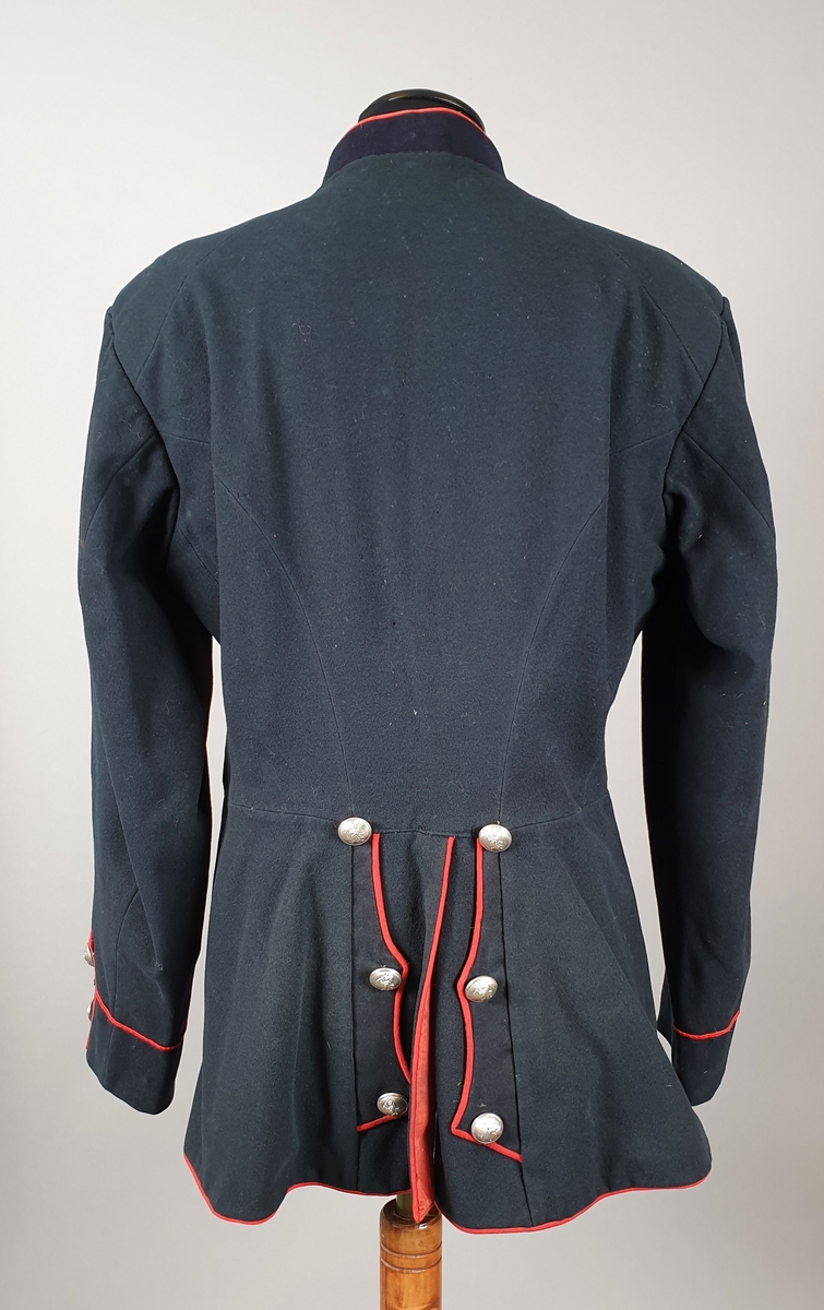 Svart uniformsjakke med røde kantbånd og rødt fôr. Metallknapper med riksvåpen i front og ytterst på ermene. Stående krage. Fôret er slit og lappet.