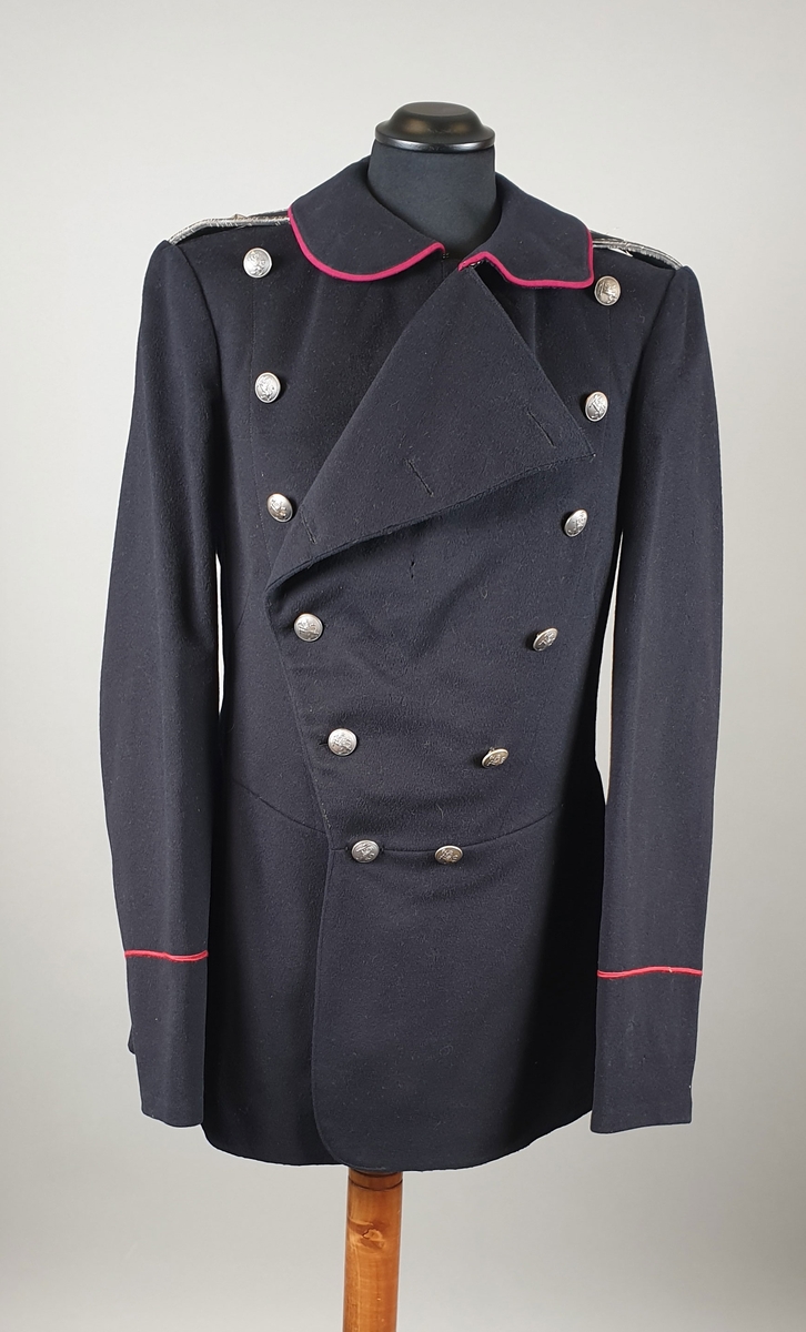 Svart uniformsjakke med mørkerøde kantbånd på krage og på ermene. Enkeltspent med metallknapper med riksvåpen. Splitt på ryggen med knapper og røde kantbånd.
