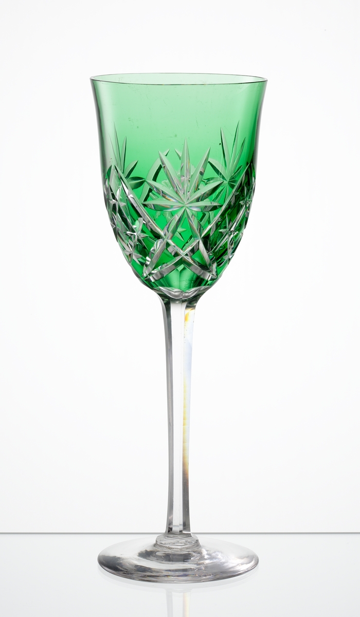 Design: Okänd. 
Rhenvinsglas,svagt klockformad, mörkgrön kupa med skärslipad dekor. Högt fasettslipat ben med slät fot.