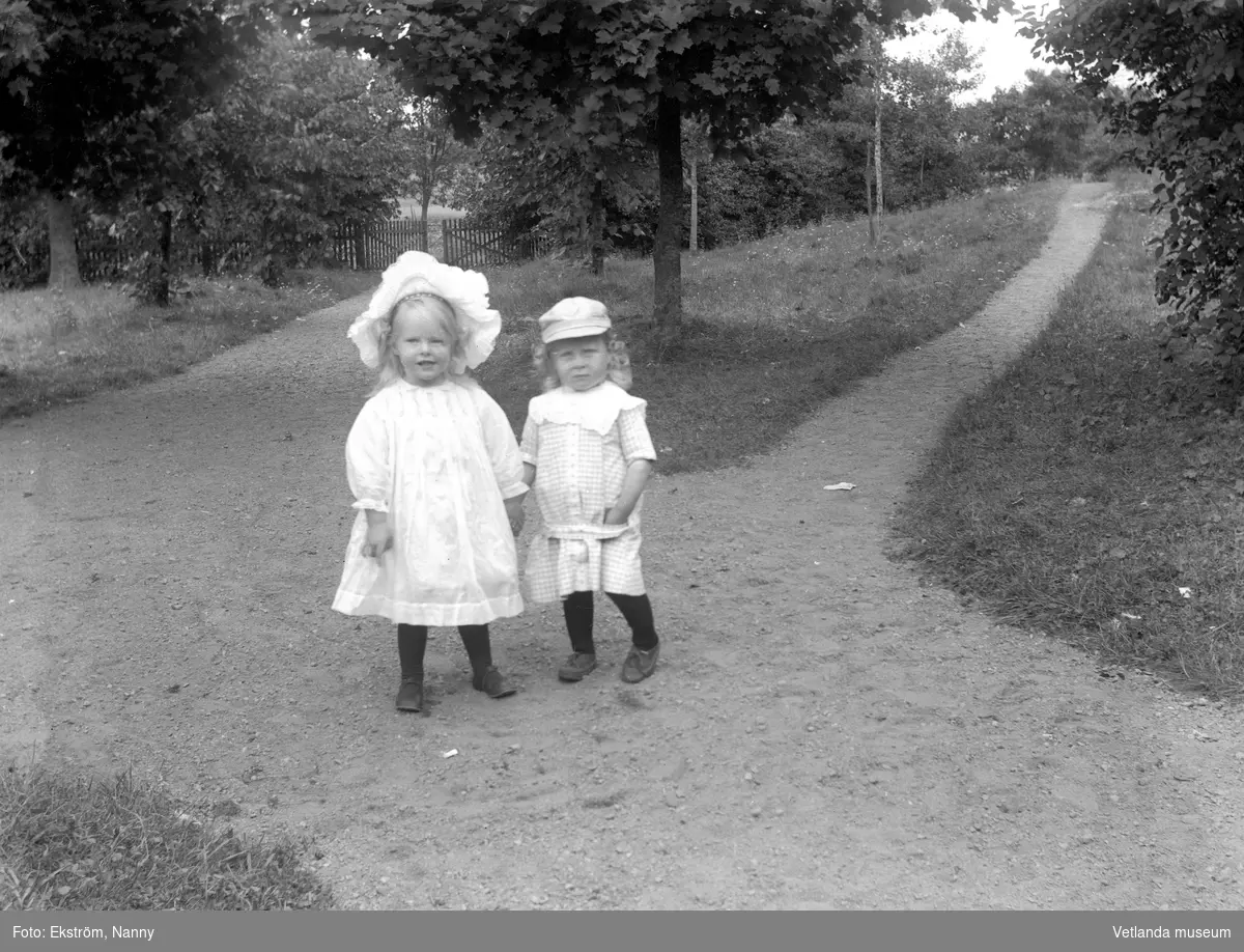 Två små barn i en trädgård eller park. Barnens anhöriga var troligtvis bekanta med fotografen.