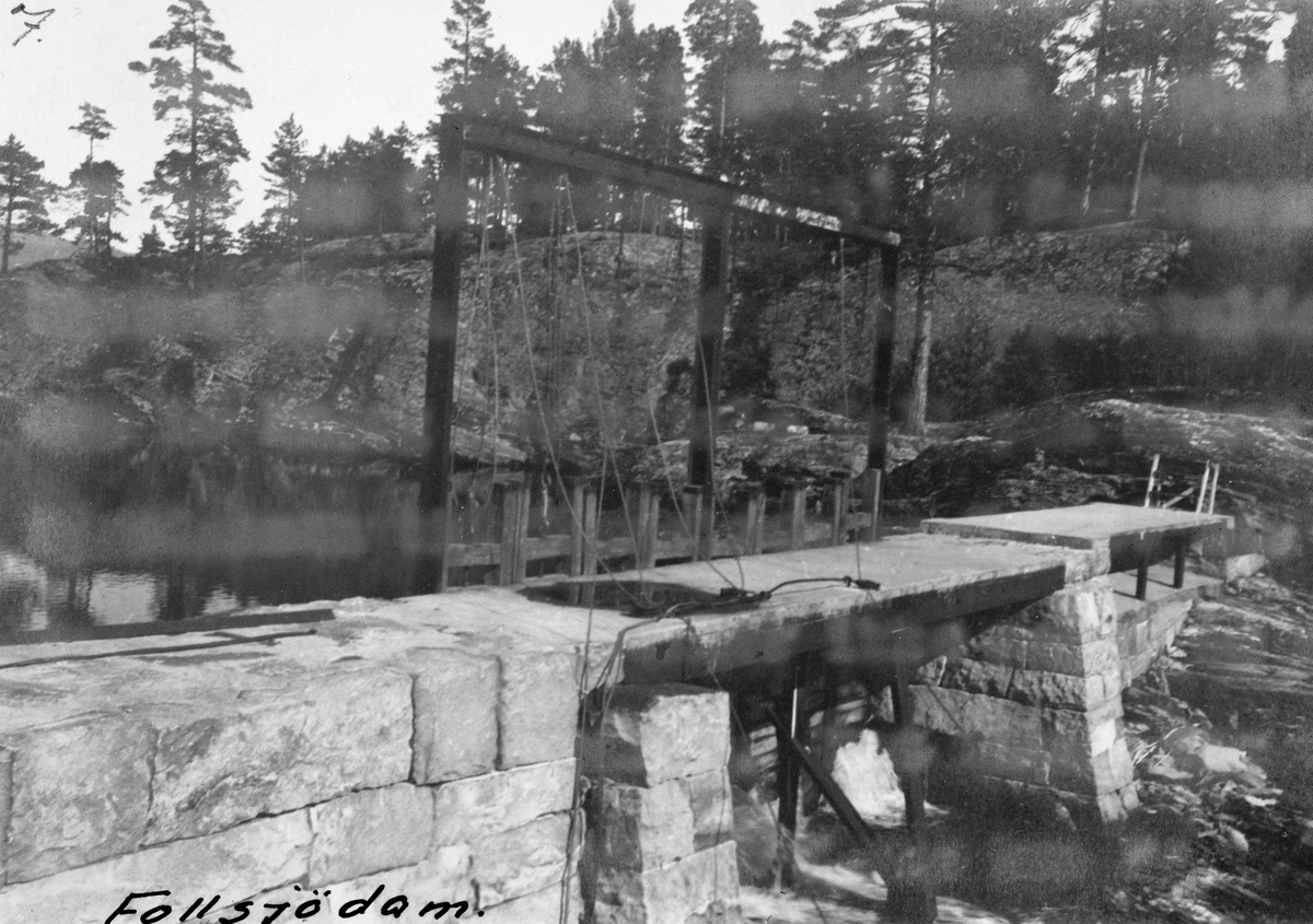 Follsjådammen eller Follsjødammen i Notodden kommune i Øst-Telemark. Den avbildete dammen ble bygd i 1912-13. Fotografiet er tatt fra en bergnabb sørvest for damstedet.  Dammen ble bygd av tilhogd naturstein, med dambru av armert betong, støpt på et underlag av stålskinner. På motstrøms side av damåpningen var det reist et stålstativ, som antakelig etter hvert skulle utstyres med trinser eller taljer, slik at det ble enklere å betjene de åtte lukene i damåpningen. Til høyre for det lukestengte løpet ser vi ei lita overløpssone.  Den avbildete steindammen avløste en steinfylt tømmerkistedam, som hadde regulert Follsjø for fløtingsformål siden 1884.  Dette fornyingsprosjektet ble for øvrig mer kostbart enn administrasjonen og styret i Skiensvassdragets Fellesfløtningsforening hadde forutsatt. For å få stein av tilfredsstillende kvalitet måtte dambyggerne foreta minering ved Vik, og deretter kjøre steinen på isen over sjøen til damstedet. Da arbeidet startet i 1912 var imidlertid isen så dårlig, at arbeidet måtte stanses og videreføres påfølgende vinter. Videre var det opprinnelig planlagt dambru av tre, men undervegs besluttet man i stedet å bruke armert betong. Dette var langt mer kostbart, men forutsattes, i motsetning til trekonstruksjoner, langt på veg velikeholdsfritt. At damstedet ble flyttet cirka tre meter oppover bidro til høyere oppdemmingsnivå, og en konflikt med grunneier O. O. Brekke, som varte i ti år og gikk gjennom alle rettsinstanser. I høyesterett endte det med at Fellesfløtningsforeningen måtte dekke saksomkostningene og betale grunneieren 500 kroner i erstatning, noe fløtingsstyret motstrebende aksepterte.