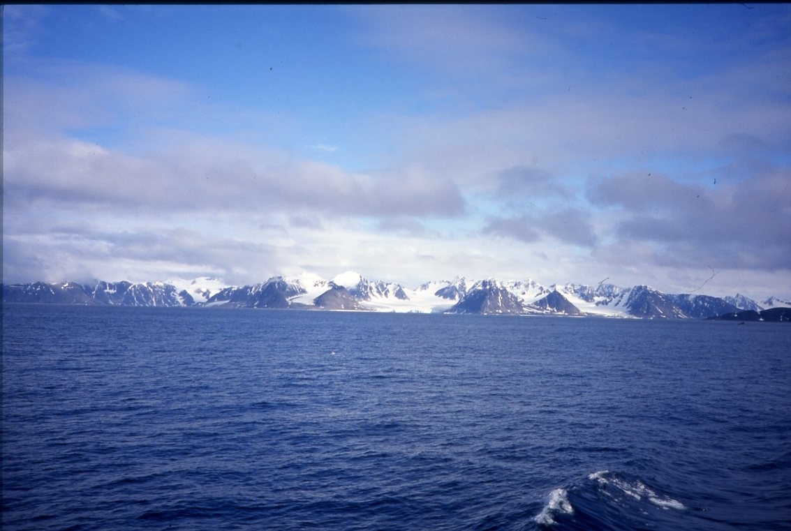 Blått hav och delvis snötäckta berg i fjärran. Troligen Spetsbergen från norr.