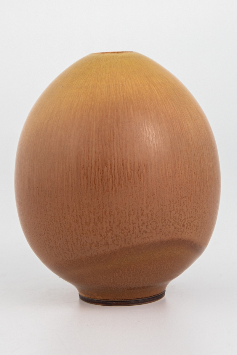 Liten eggformet vase med lav fot. Dreid steingods glasert med gulbrun harepelsglasur.