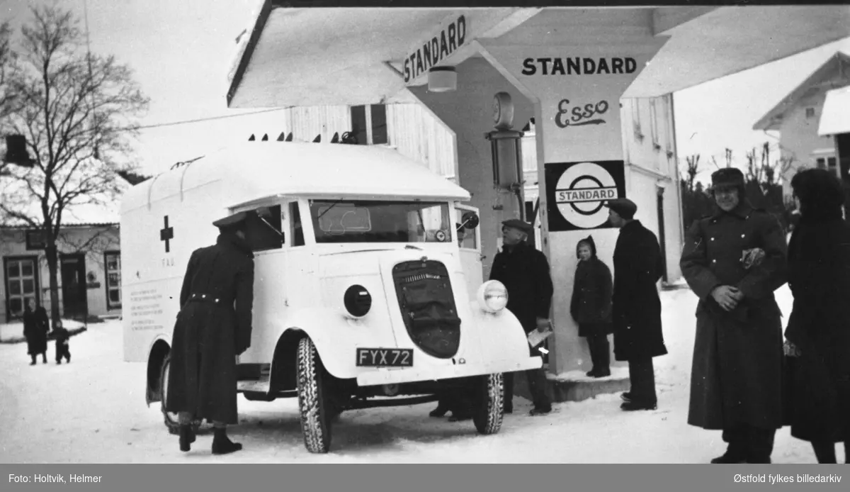 Røde Kors-bil som er underveis til Finland under stopp på bensinstasjon i Ørje, Marker 1939. Bil av merket engelsk Ford lastebil modell 7V 1937-39, bilkjennetegn FYX 77.
Reklame for Standard Esso.