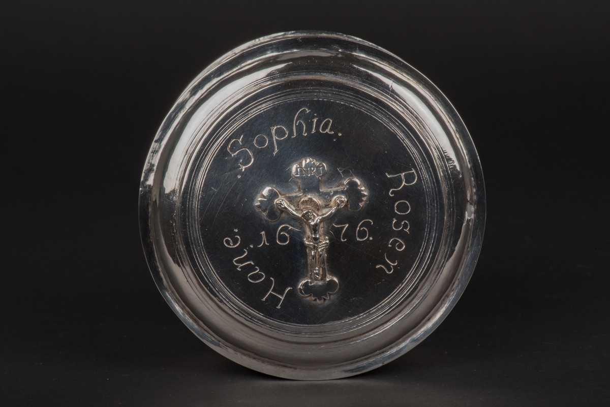 Rund oblatask med lock av silver.
Locket är dekorerat med ett krucifix och runt detta en inskription "Sophia. Rosen Hane. 1676.
Två otydliga silverstämplar på askens undersida.
