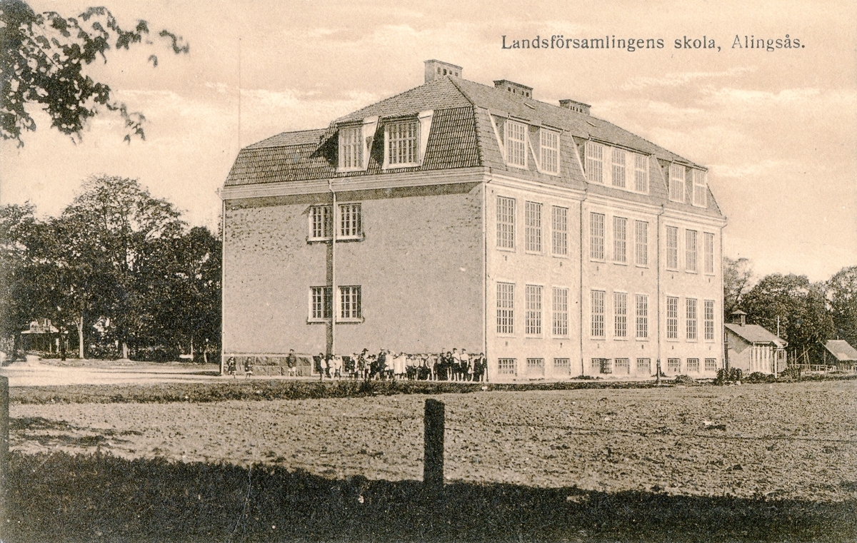 Vykort av Landsförsamlingens skola, invigt 1917, nu Afzeliiskolan. Skolbyggnaden, en samling elever och andra står utanför skolan.