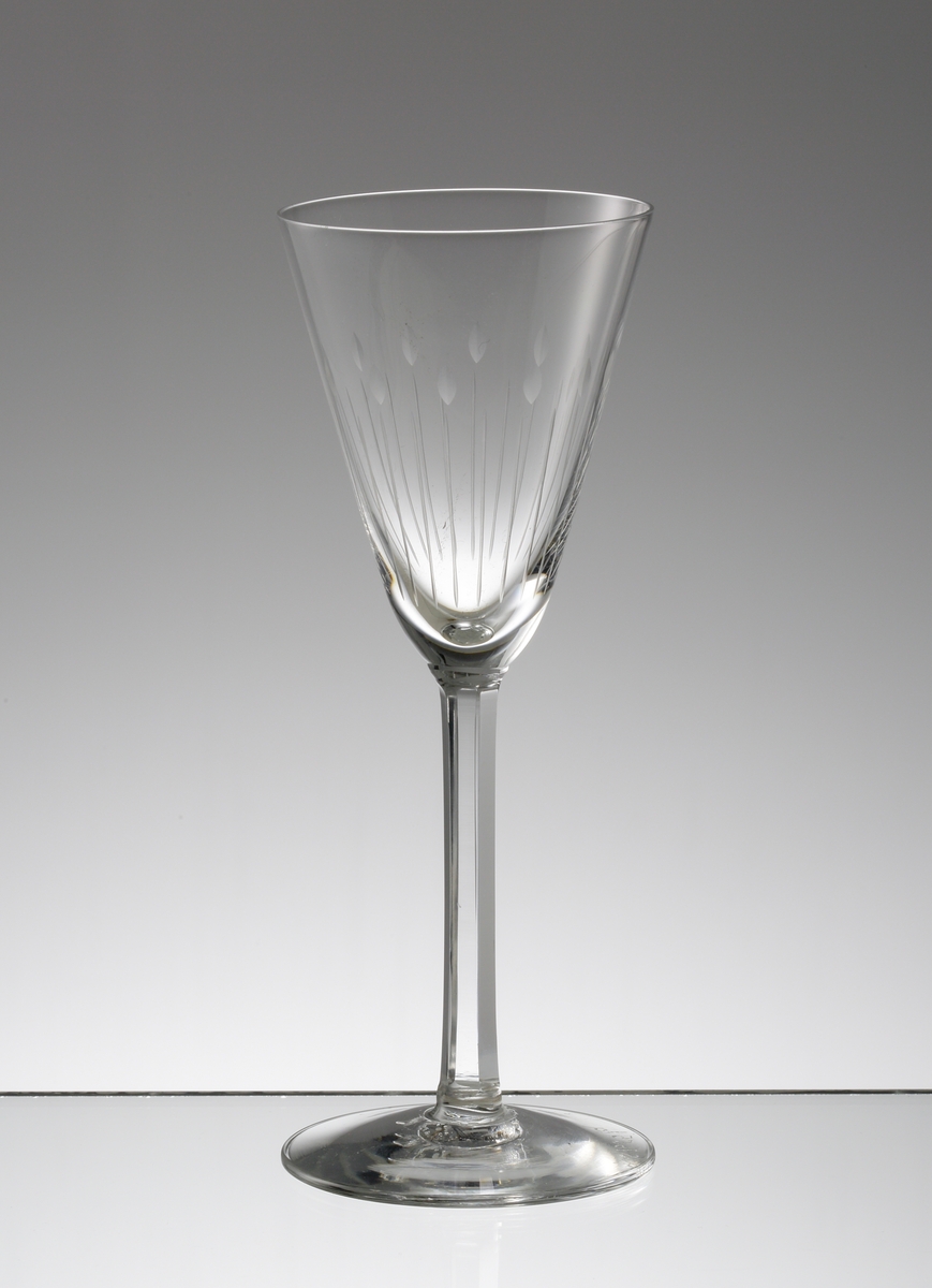 Design: Nils Landberg.
Brännvinsglas. Konande kupa med fasettslipat ben. Graverad stiliserad dekor på nedre delen av kupan.