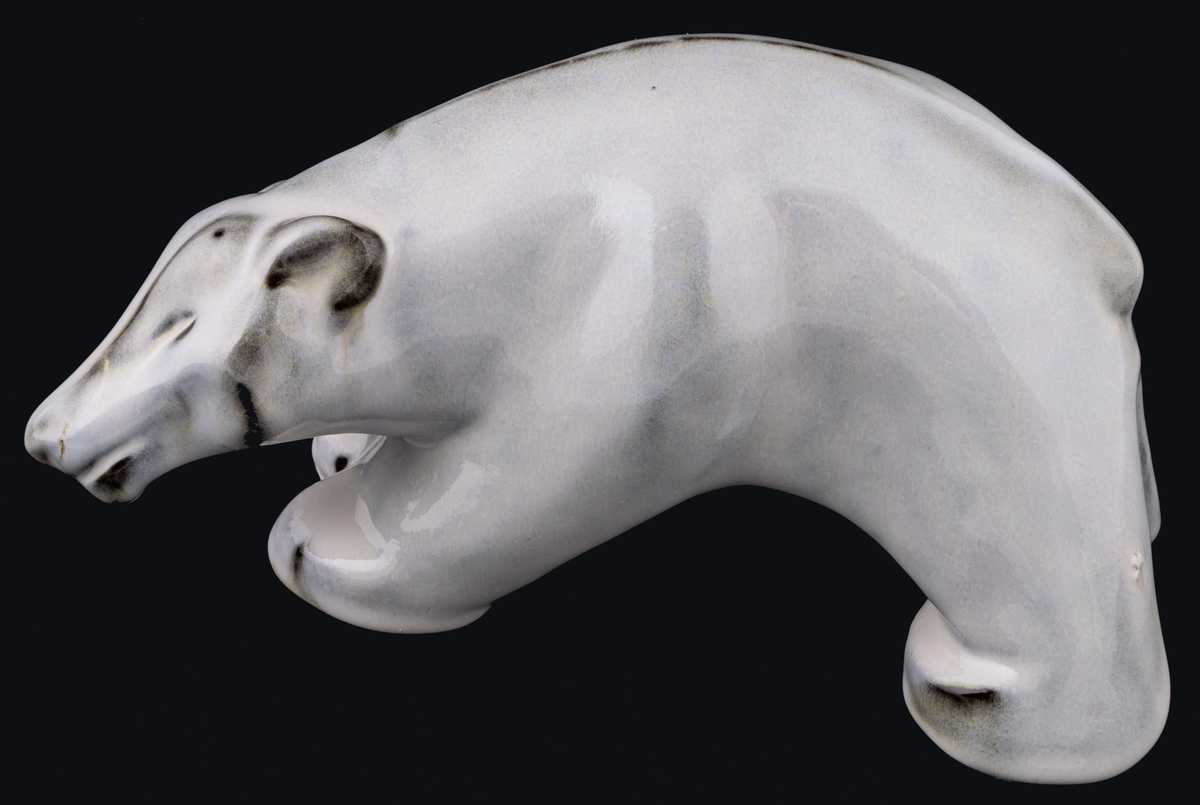 Figurin föreställande stående isbjörn, röd stengodslera, vit blank glasyr. Formgiven av Maggie Wibom för Gefle 1933-43, signerad med initialer på höger bakben. Inga fabriksstämplar.