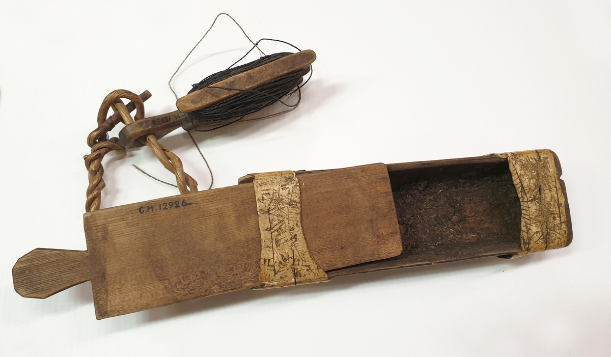 Masklåda med metrev. Lådan märkt 1843, ALS, samt bomärke.
Lådan smal med skjutlock och med näverbeslag.
Vidhängande i kort vidjelänk en liten vinda av trä med reven virad.