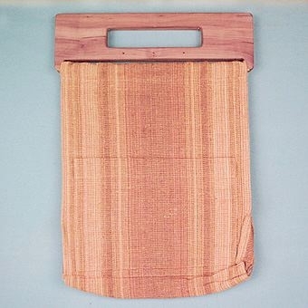 Väska sydd av cottolinlöpare "Umeå", 40 cm bredd. Sydd som en rak påse med 10 cm breda sidostycken och botten, ficka med måtten 265 x 185 mm påsydd på utsidan. Öppningens kortsidor är kantade med gult bomullsband. Väskan är monterad på en bärbygel av sälgträ.