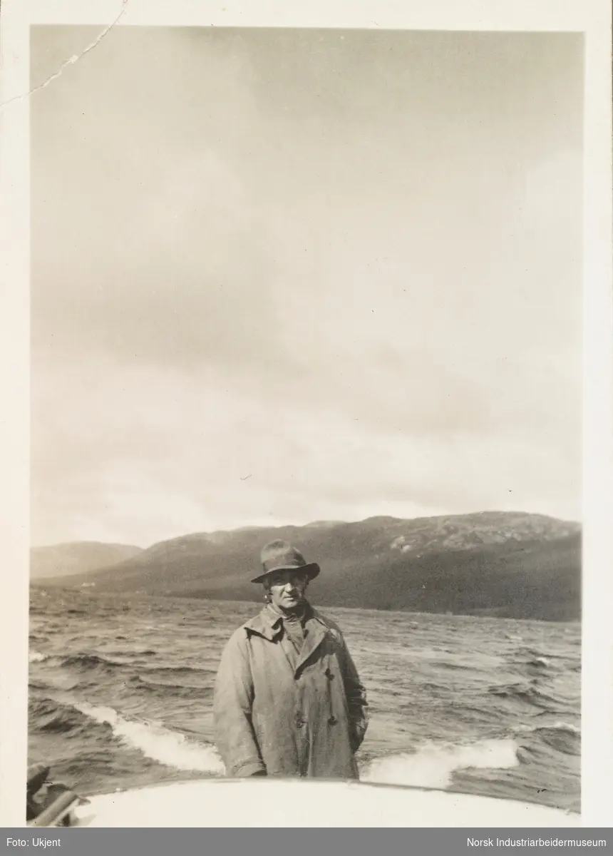 Tur til Møsvand, høsten 1931. Jens Poulsson med frakk og hatt står på båt på Møsvatn. Fjellside i bakgrunn.