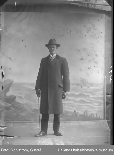 Mansporträtt av banvakt HM Svensson, stående i helfigur, ateljéfoto. Mannen är klädd i rock och hatt.