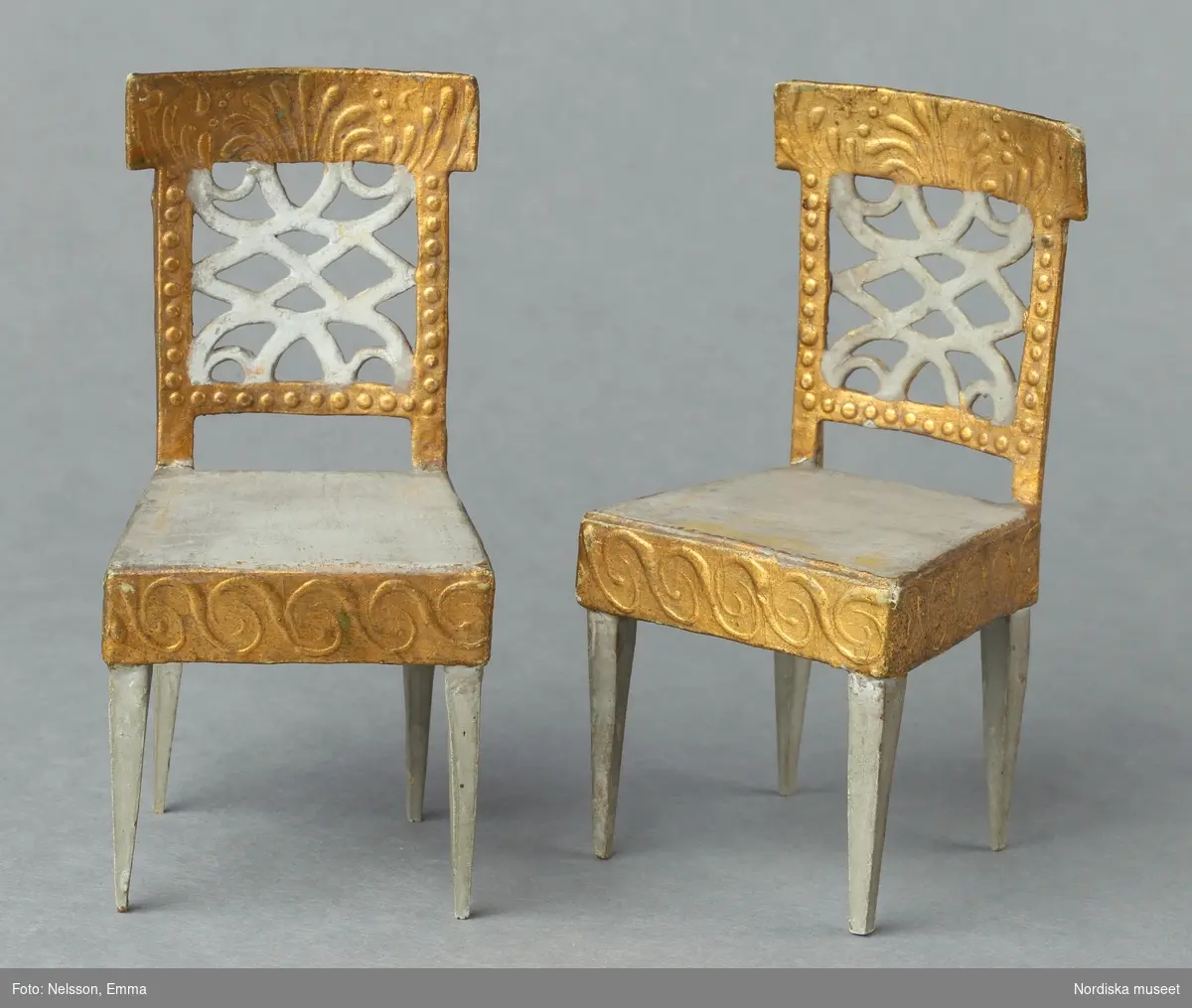 Inventering Sesam 1996-1999:
H 11,5 cm
4 st stolar till dockskåp tillverkade av trä, papp och massa. Fyra rakt nedåt avsmalnande ben av trä, fyrkantig gråmålad sits, sarg och fyrkantigt genombrutet ryggstöd av papp och massa med reliefmönster i guld och vitt.
Hör till dockskåp 165.280
Bilaga
Leif Wallin 1996