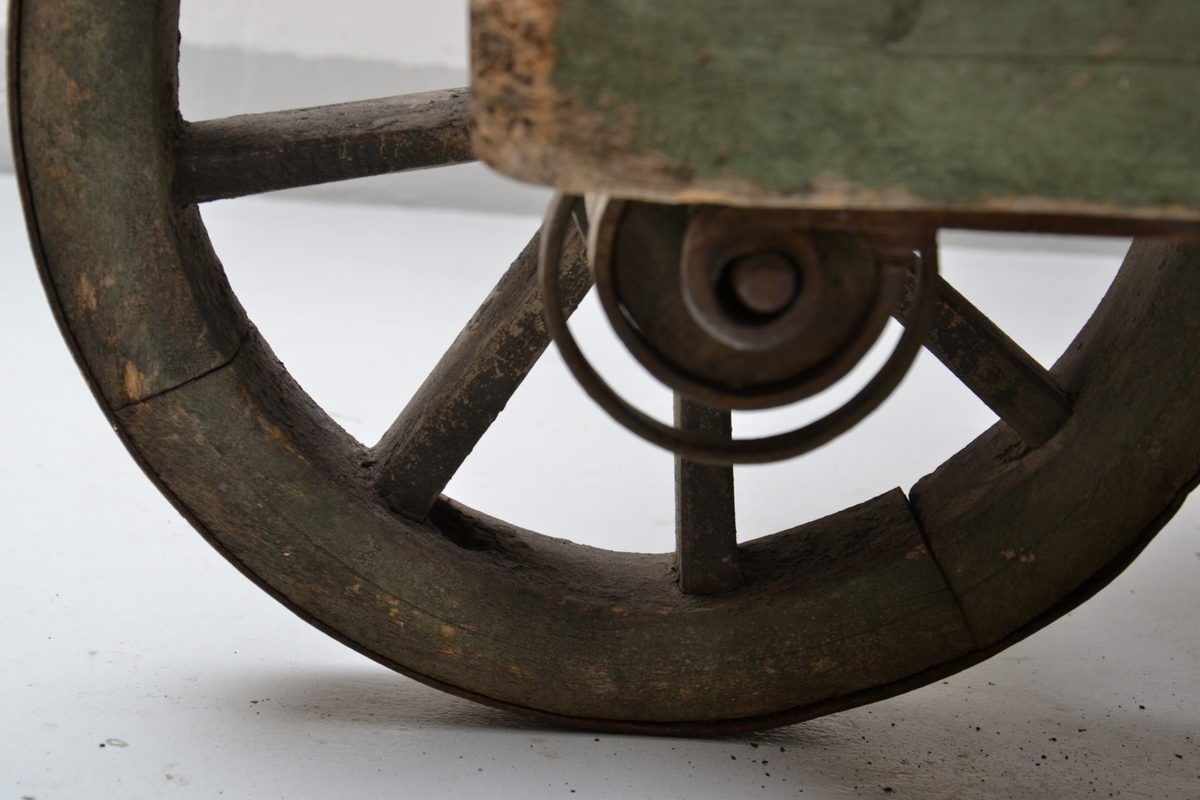 En opprinnelig grønnmalt trillebår i tre med et jernbeslått hjul. Den ene siden har en yngre reperasjon.