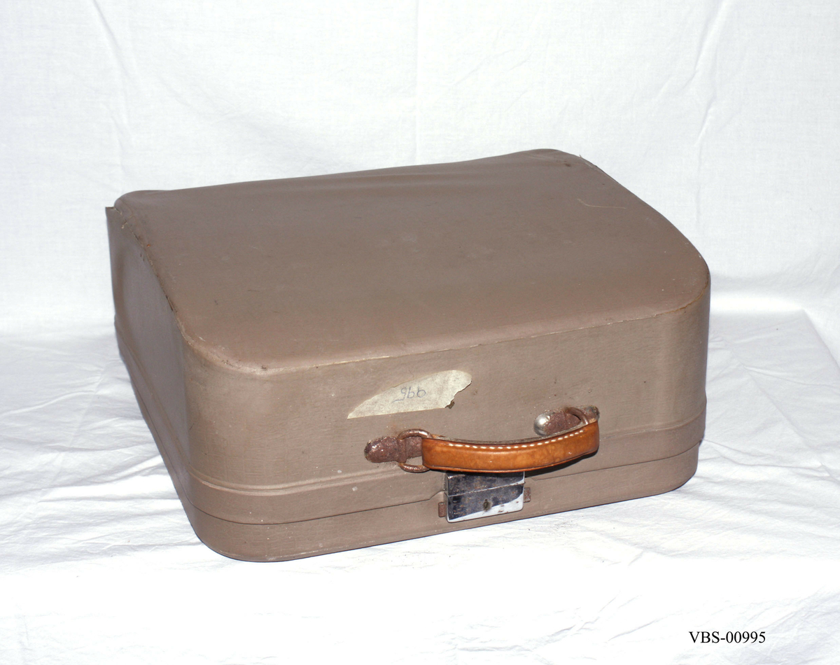 Reiseskrivemaskin i koffert.
Transportabel skrivemaskin i metall og plast. Skrivemaskinen er fastmontert i koffertbunnen, men kan den tas ut av kofferten. Den har avtagbart lokk med bærehåndtak i lær. Nøkkelløs lås.