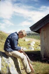Bjørn Dyrland renser et gevær mellom bena mens sitter på en 