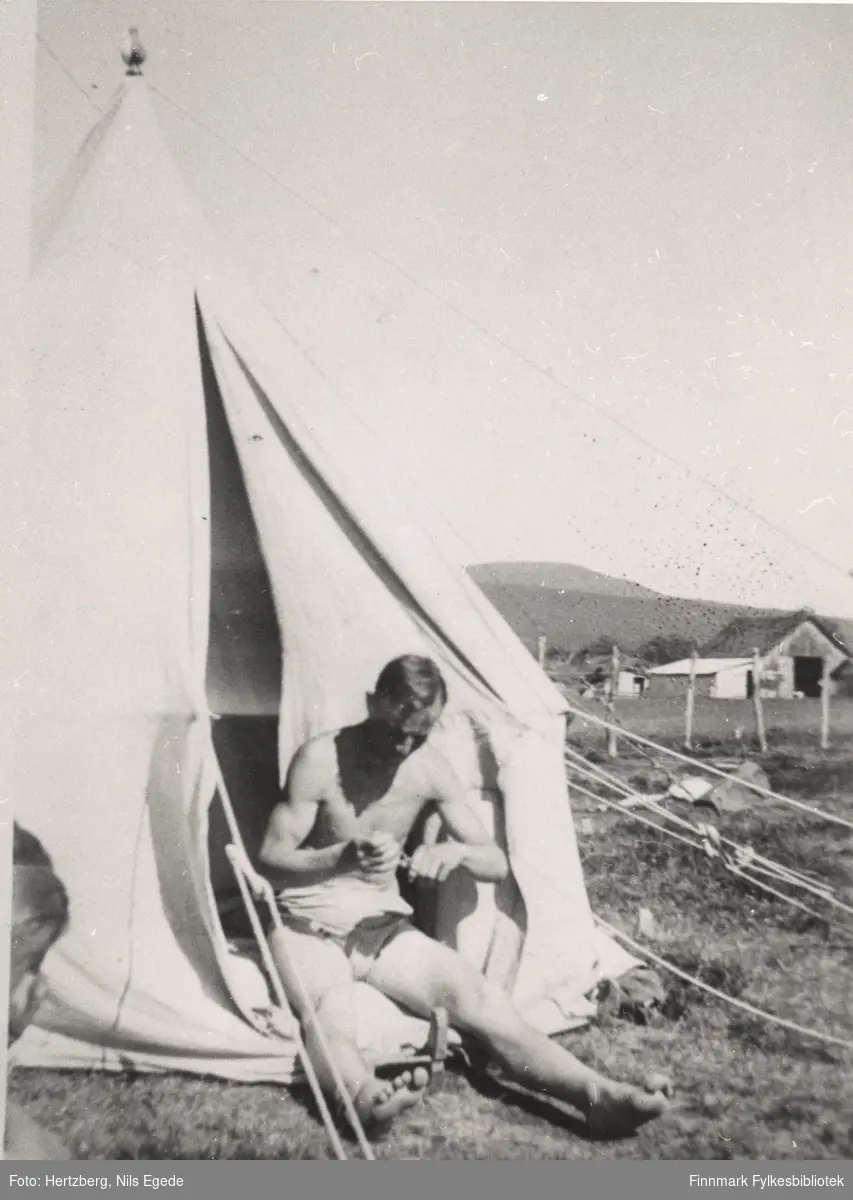 En mann utenfor teltet sitt. Byggearbeid foregår ved Seida fergested, Tana, i 1939.
