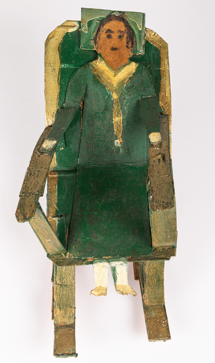 Skulptur av papp, oljefärg och troligen lackfärg. Föreställer grönklädd kvinna i gungstol. Målad i grönt och guld.