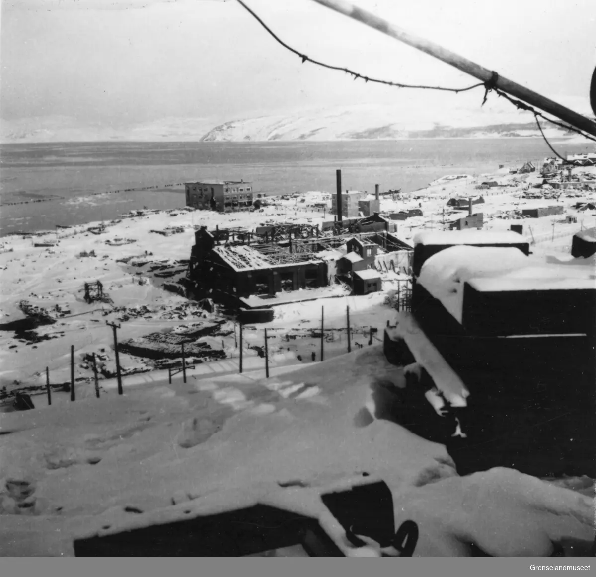 Utsikt fra Sydvarangers anlegg over byen og fjorden, midt i bildet ser vi ruiner av dampsentralen og betongskolen, vinteren 1944/45.