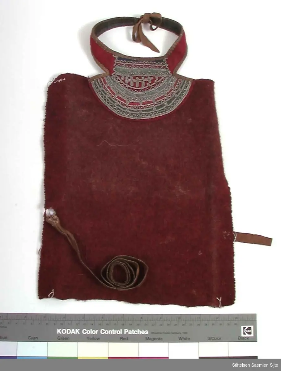 Rødt brystklede med tekstilapplikasjoner og rik tinntråddekor ved kragen, samt skinnreimer og skinnlinning i kragen og til feste i sidene av kledet.