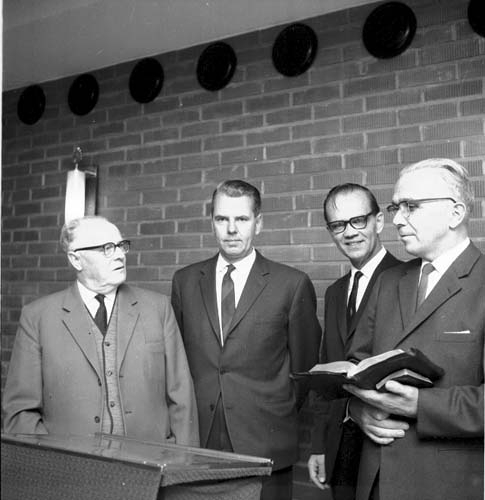 Fyra män i mörka kostymer står uppradade runt ett talarbord. En man, Robert Svensson, håller två böcker i handen, eventuellt en bibel och en psalmbok. Intill honom står Olof Nilsson.