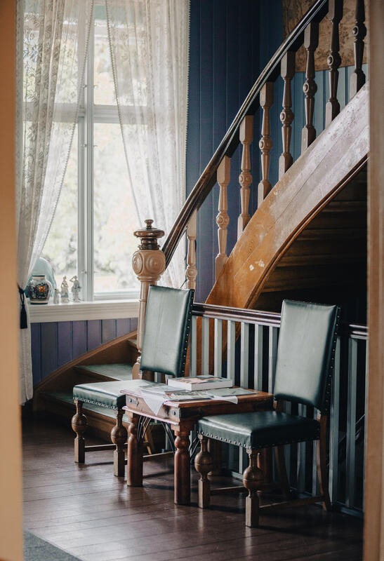 Bilde av entre med trapp opp. Bord med to stoler og bord i mellom står ved trappen.